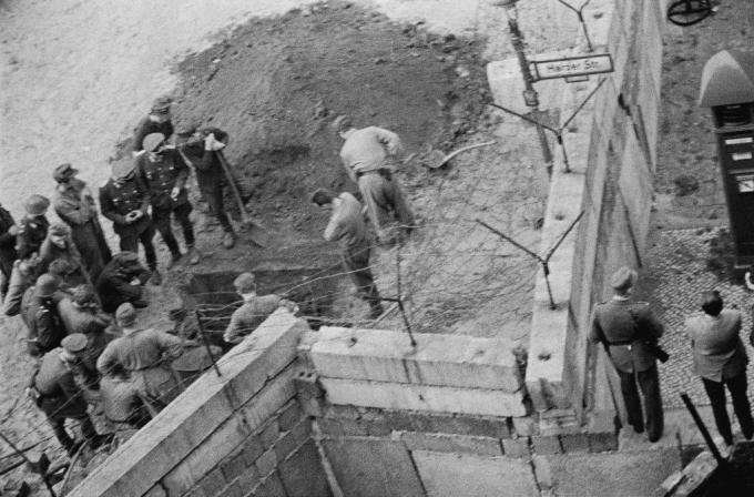 Skupina východonemeckých vojakov skúma vykopaný tunel pod berlínskou stenou.