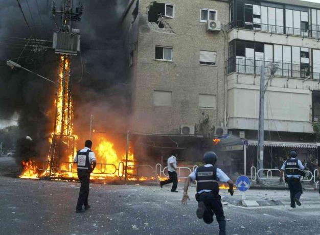 Izraelskí policajti sa ponáhľajú na scénu horiaceho elektrického stožiara a poškodia stavebné okamihy, keď 13. júla 2006 zasiahla v severnom meste Nahariya v izraelskom meste Nahariya izraelská raketa Hizballáhu.