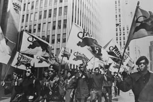 Čierne dychtenie pochodujúce s vlajkami počas protestu Huey zadarmo.