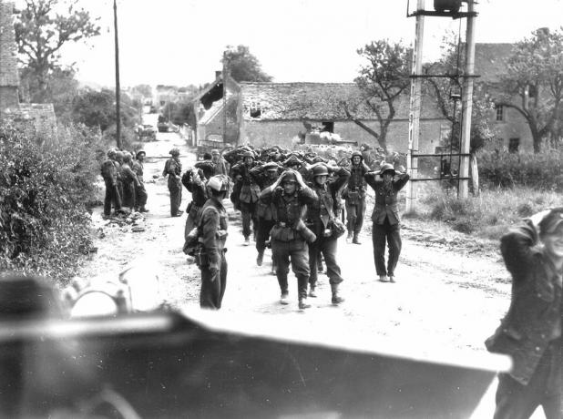 Nemeckí vojaci pochodujú po ulici s rukami na hlavách v kapitulácii.